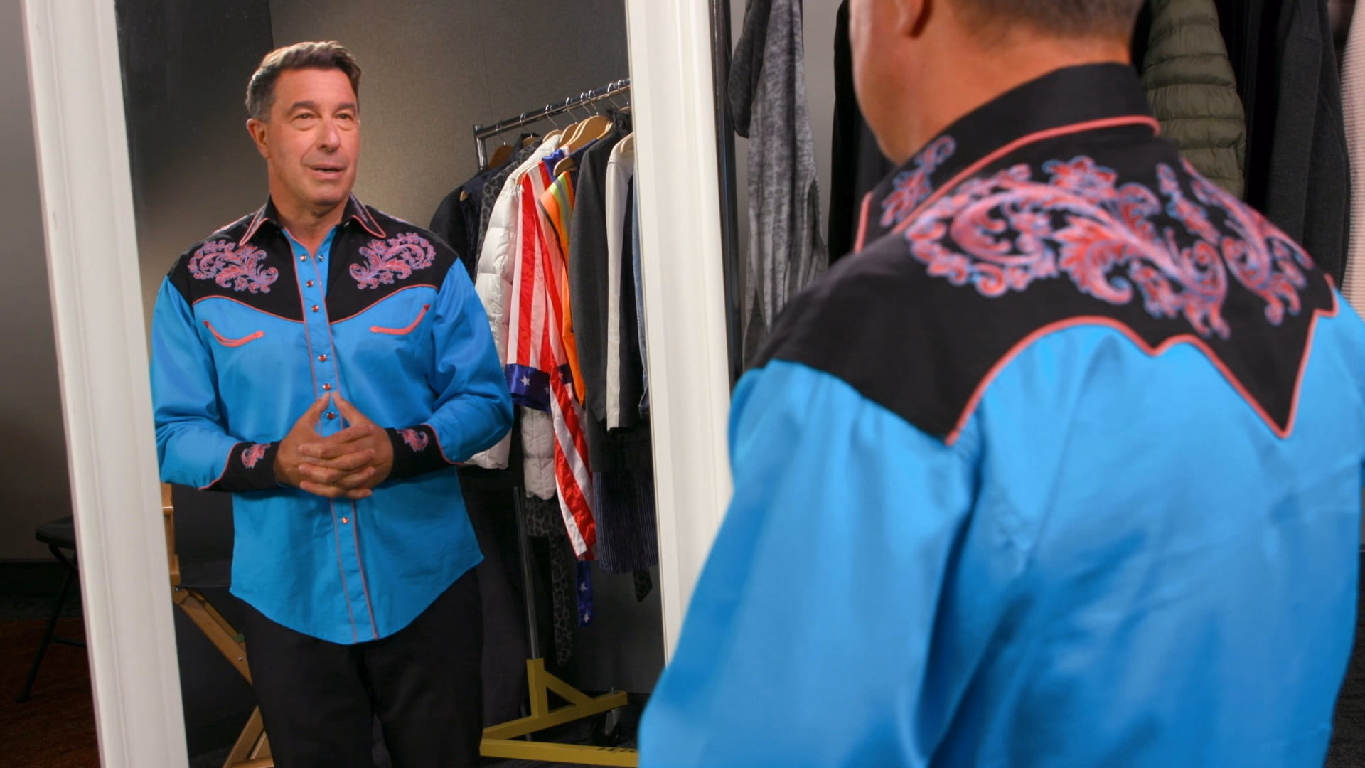 A guest in an embroidered western shirt considers his reflection in the wardrobe mirror